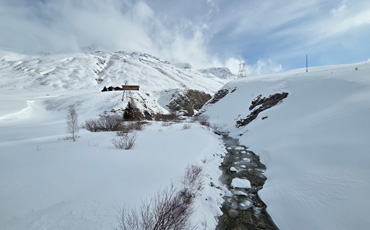  „Verschneite Berglandschaft bei Juf in Graubünden mit kleinem Bach, Holzhütte und klarer Wintersonne.