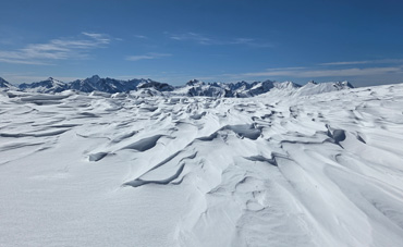 Verschneite Hochgebirgslandschaft bei Juf in Graubünden mit bizarren Schneeverwehungen unter klarem blauem Himmel.